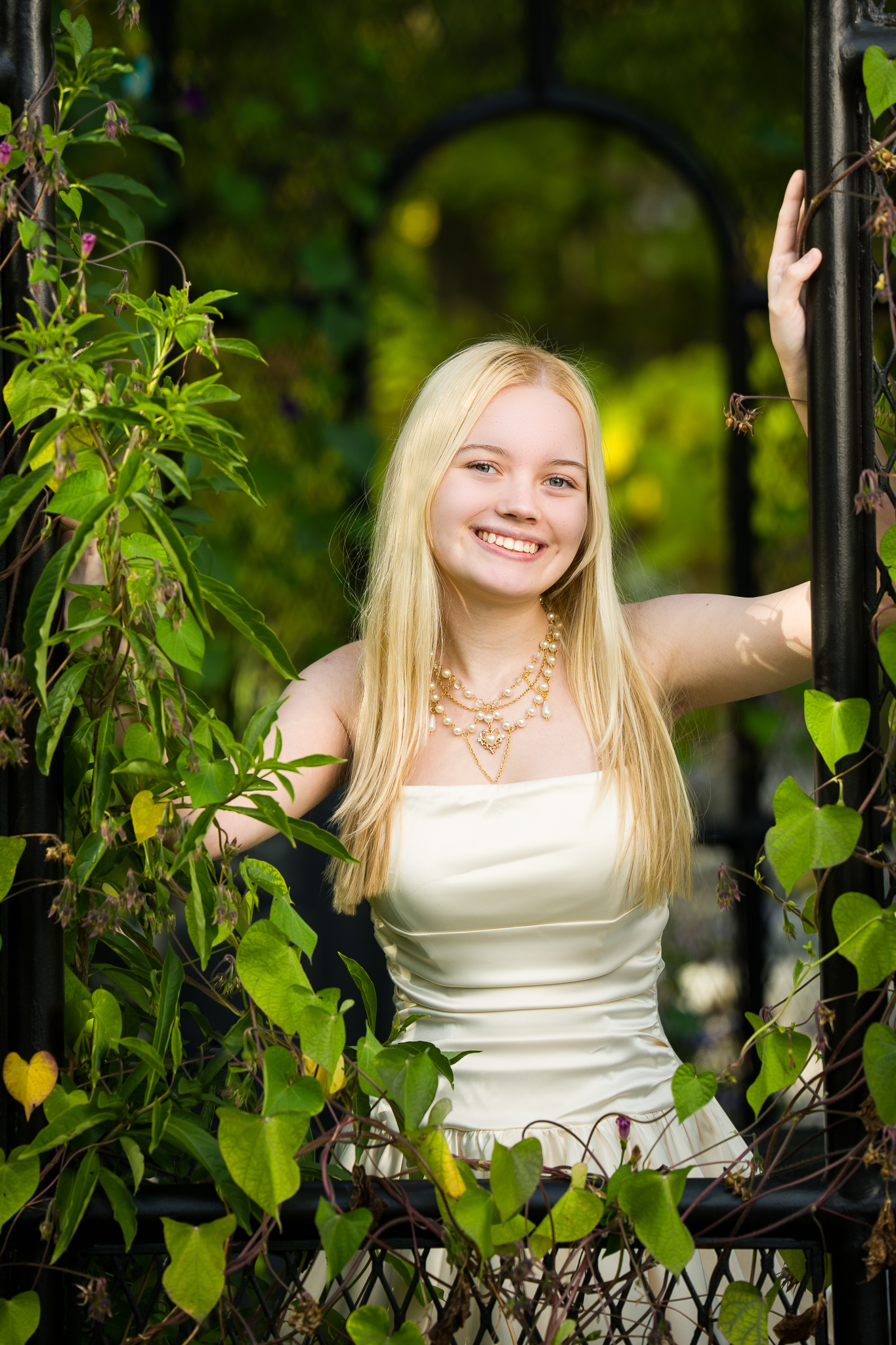 Blonde senior girl in a cream top in a garden gazebo wrapped in vines, senior portrait in Tower Hill Botanic Garden, Boylston, MA