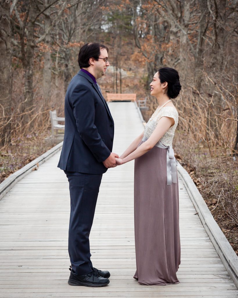 Couple holding hands facing each other on a wooden boardwalk, wedding portrait in Boylston, MA