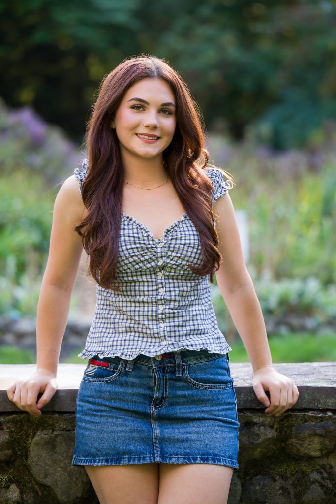 High school girl leaning against rock wall smiling and in a relaxed pose, senior portrait session in Shrewsbury, MA.