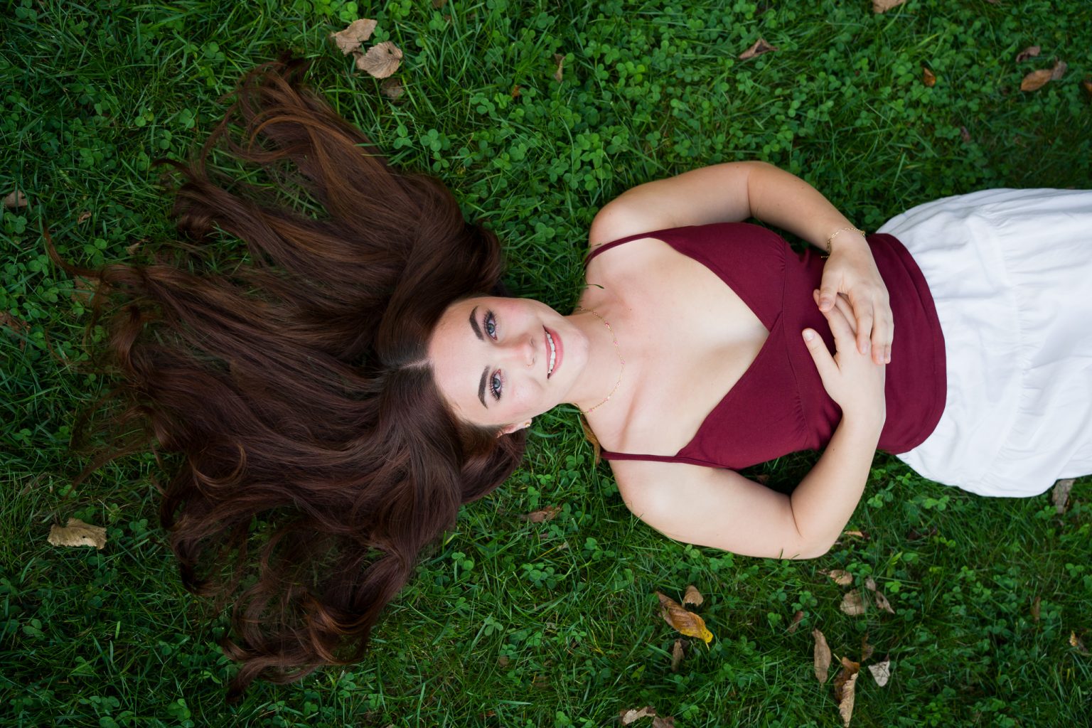 Senior lying on the grass smiling up at the camera, senior portrait at Garden of Sweet Remembrance, Shrewsbury, MA