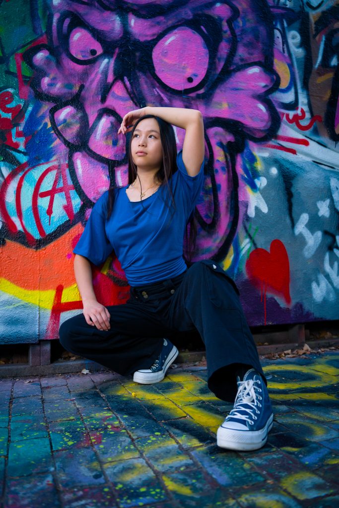 Senior girl in a blue top and sneakers posing against a colorful graffiti wall, urban senior portrait in Graffiti Alley, Cambridge, MA