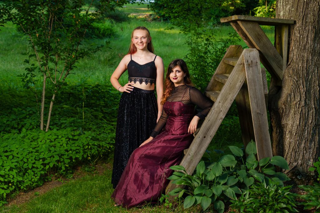 Two teen girls in formal dresses beside a wooden ladder on a lawn, prom portrait in Shrewsbury, MA