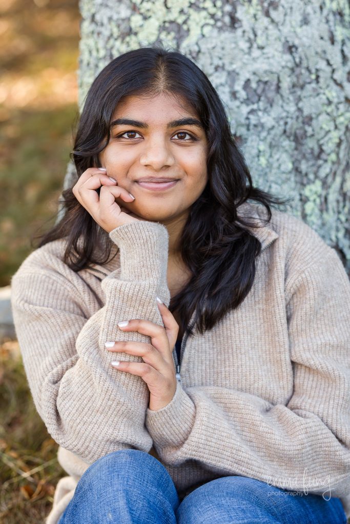 Senior girl in a cream sweater resting her chin on her hand by a tree, senior portrait in Great Brook Farm State Park, Carlisle, MA