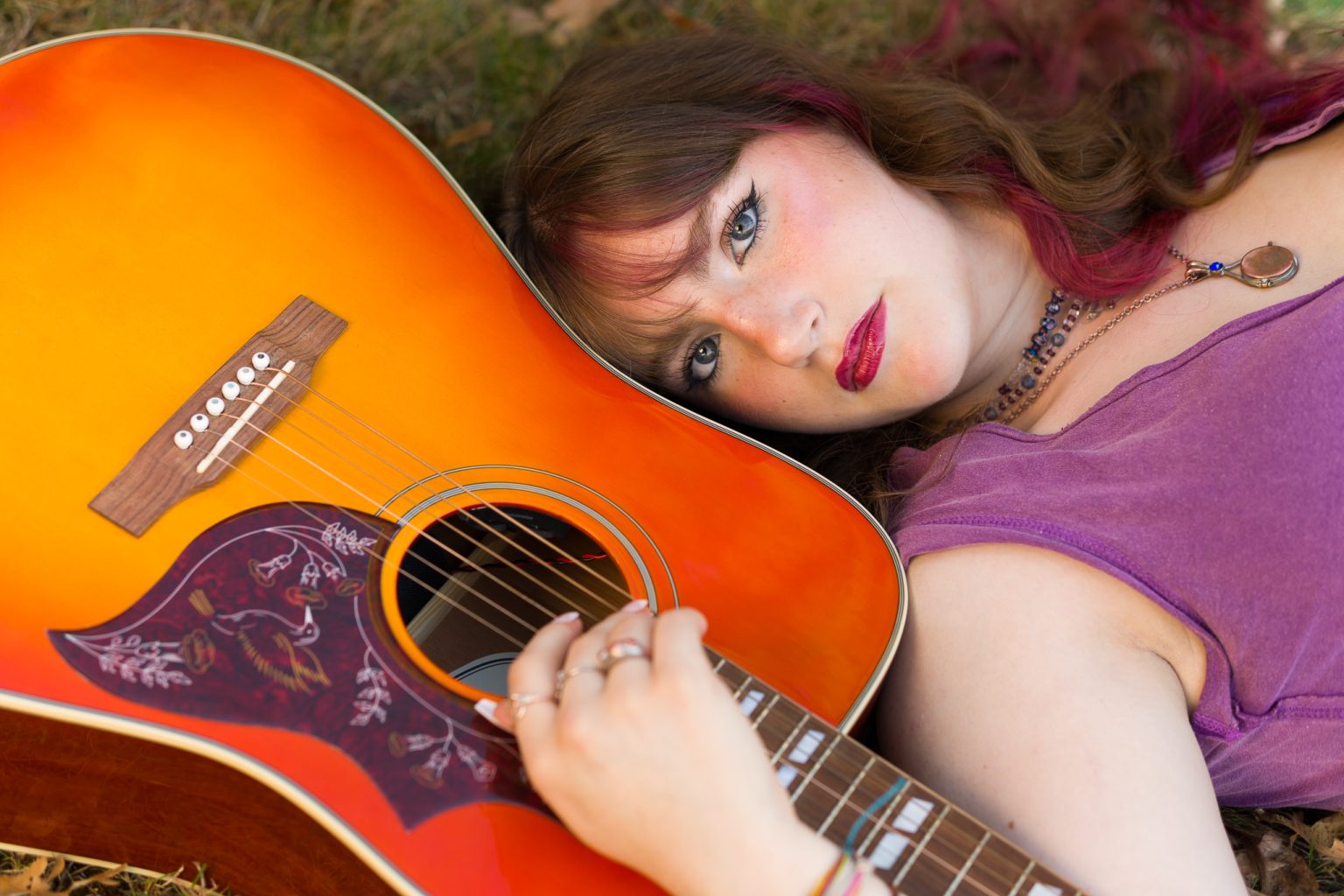 Senior lying in the grass with head resting on an orange acoustic guitar, senior portrait at Dean Park, Shrewsbury, MA