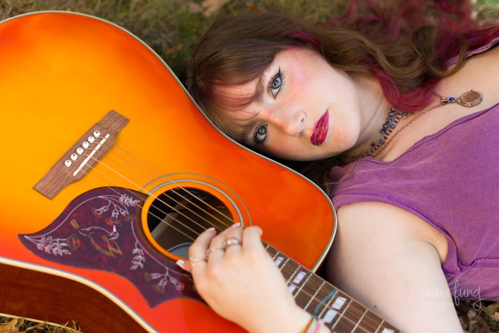 Senior lying in the grass with head resting on an orange acoustic guitar, senior portrait at Dean Park, Shrewsbury, MA