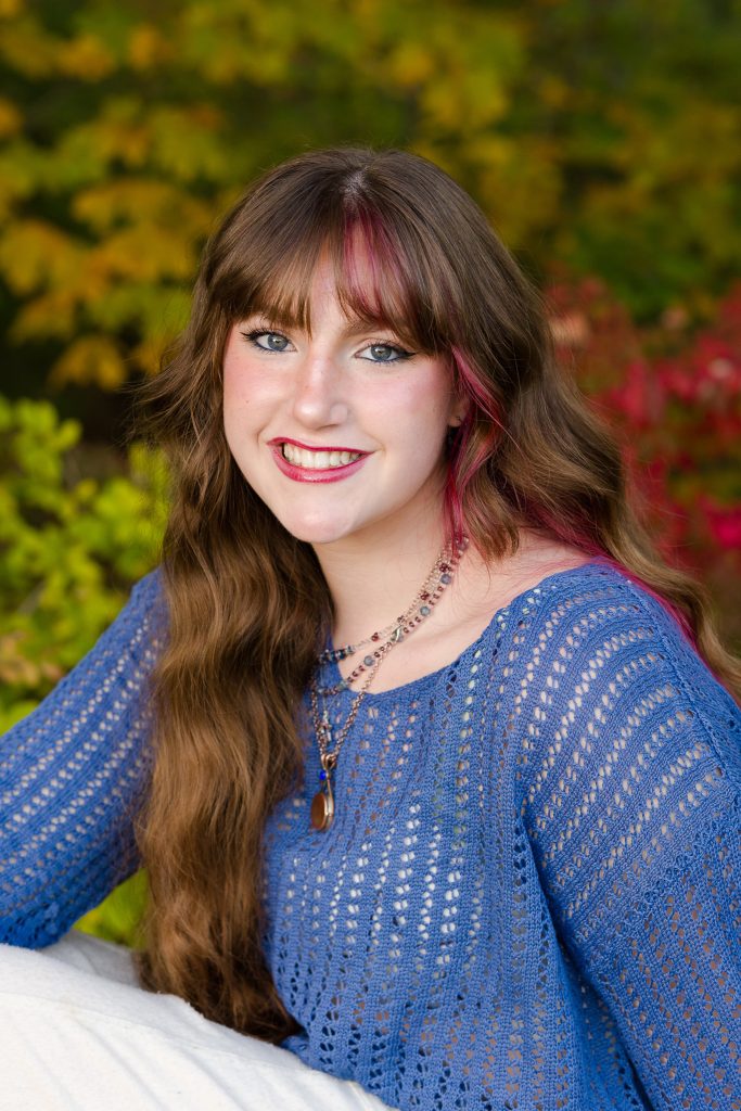 Senior girl with long wavy hair in a blue knit top smiling at the camera, senior portrait in Dean Park, Shrewsbury, MA