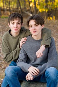 Two teenage brothers sitting together outdoors in golden fall light, sibling portrait in Dean Park, Shrewsbury, MA