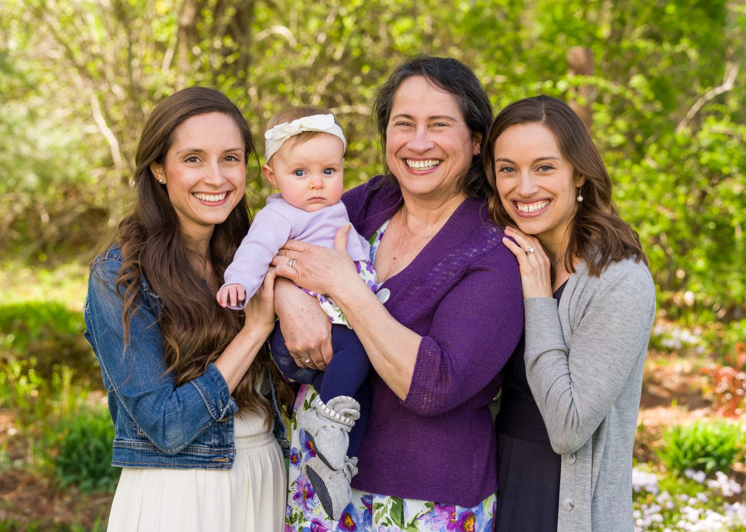 Three smiling women holding a baby in a spring garden, family portrait at home in Northborough, MA