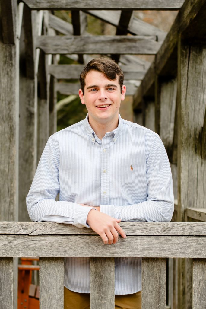 Senior guy in a light button-down leaning on a weathered wooden railing, senior portrait in Moore State Park, Paxton, MA