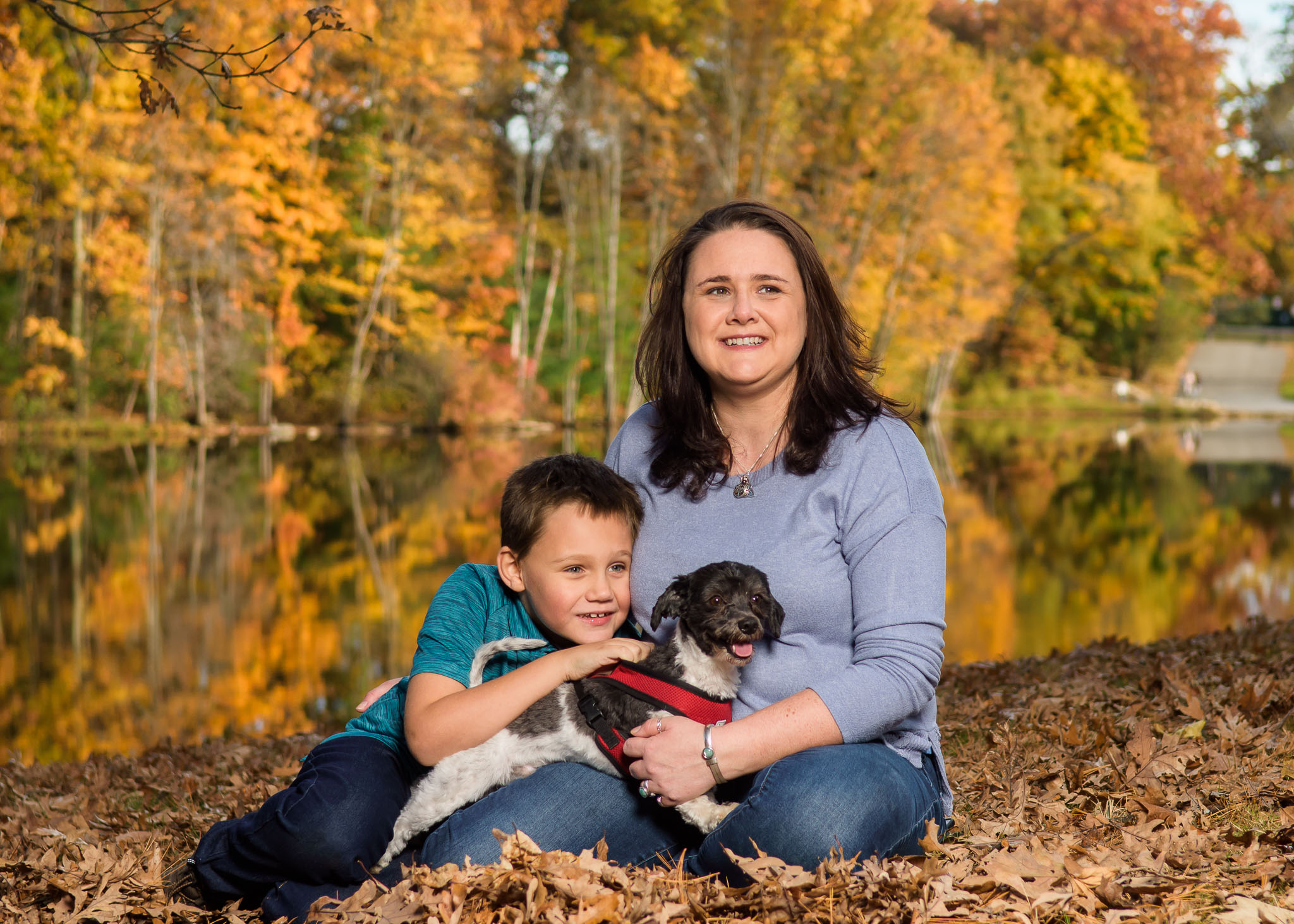 Mother with young son and small dog among fall leaves by a lake, family portrait session in Dean Park, Shrewsbury, MA