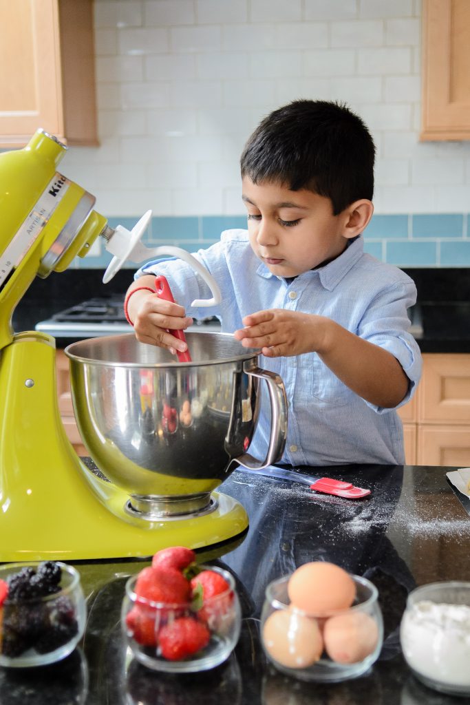 A South Asian little boy scraping the bowl of an electric stand mixer, family portrait session in Shrewsbury, MA. 