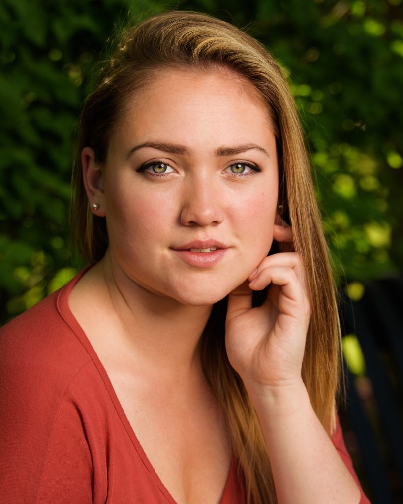 Headshot of a young woman in a rust top with her hand at her cheek, Greenhill Park, Worcester, MA