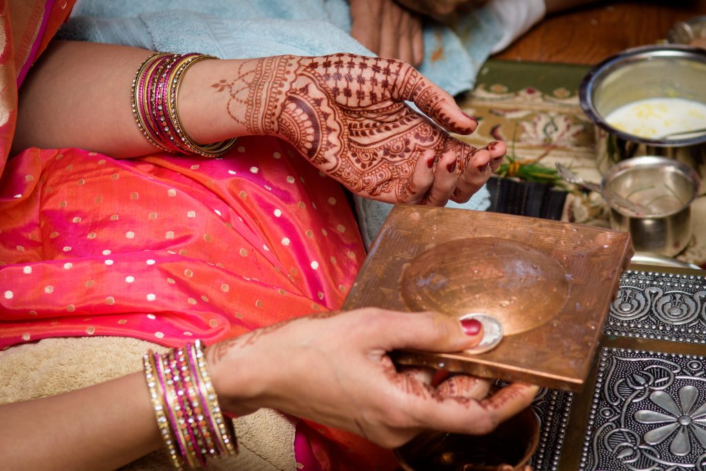 Henna-decorated hands holding a copper dish during a traditional Indian ceremony, event photography at a client's home in Shrewsbury, MA