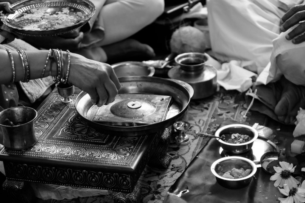 Black-and-white close-up of brass bowls and a ceremonial plate during an Indian ritual, event photography at a client's home in Shrewsbury, MA