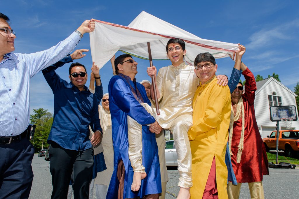 Relatives holding a white canopy over a man in cream and yellow Indian attire, wedding celebration in Shrewsbury, MA
