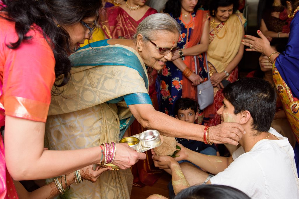 Elder woman in a sari performing a traditional ritual as family gathers around, Indian celebration in Shrewsbury, MA