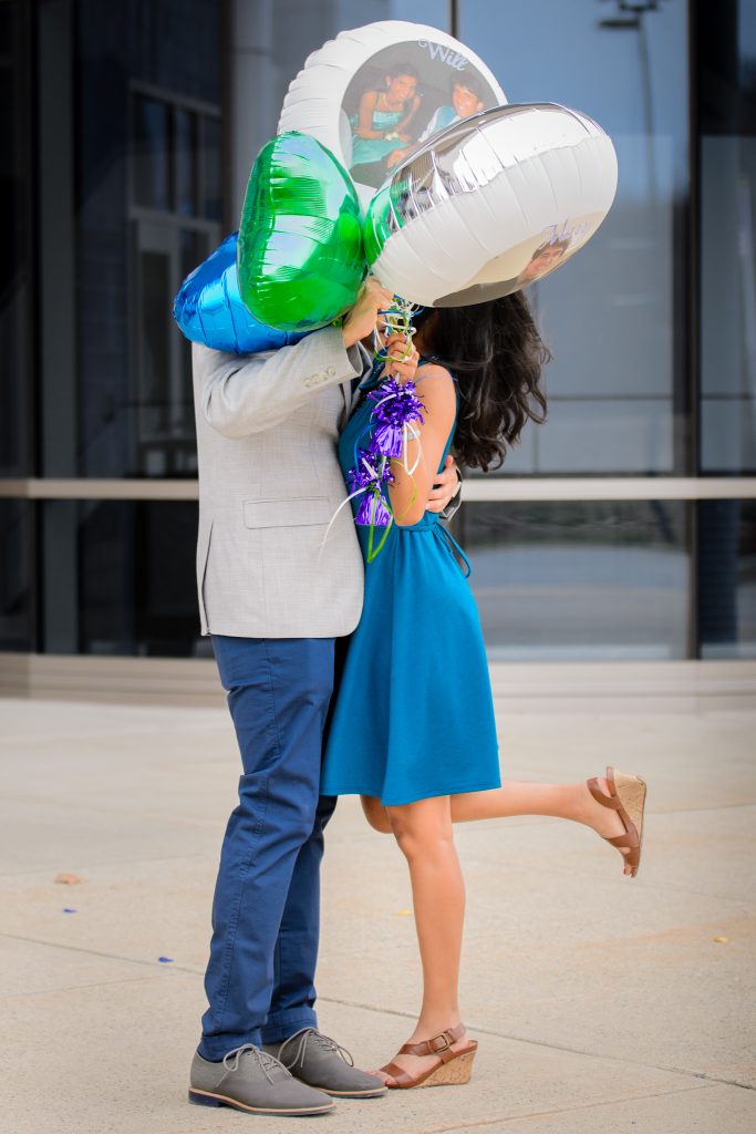 An engagement photo of a South Asian man and woman in an embrace with their faces hidden behind four foil balloons, engagement portrait session in Shrewsbury, MA. 