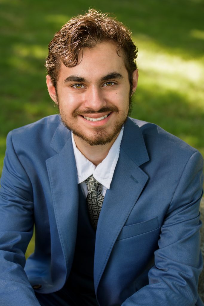 Young man in a blue suit jacket smiling outdoors, senior portrait in Dean Park, Shrewsbury, MA