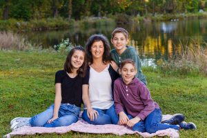 Mother and three children sitting on a picnic blanket by a pond, family portrait session in Dean Park, Shrewsbury, MA