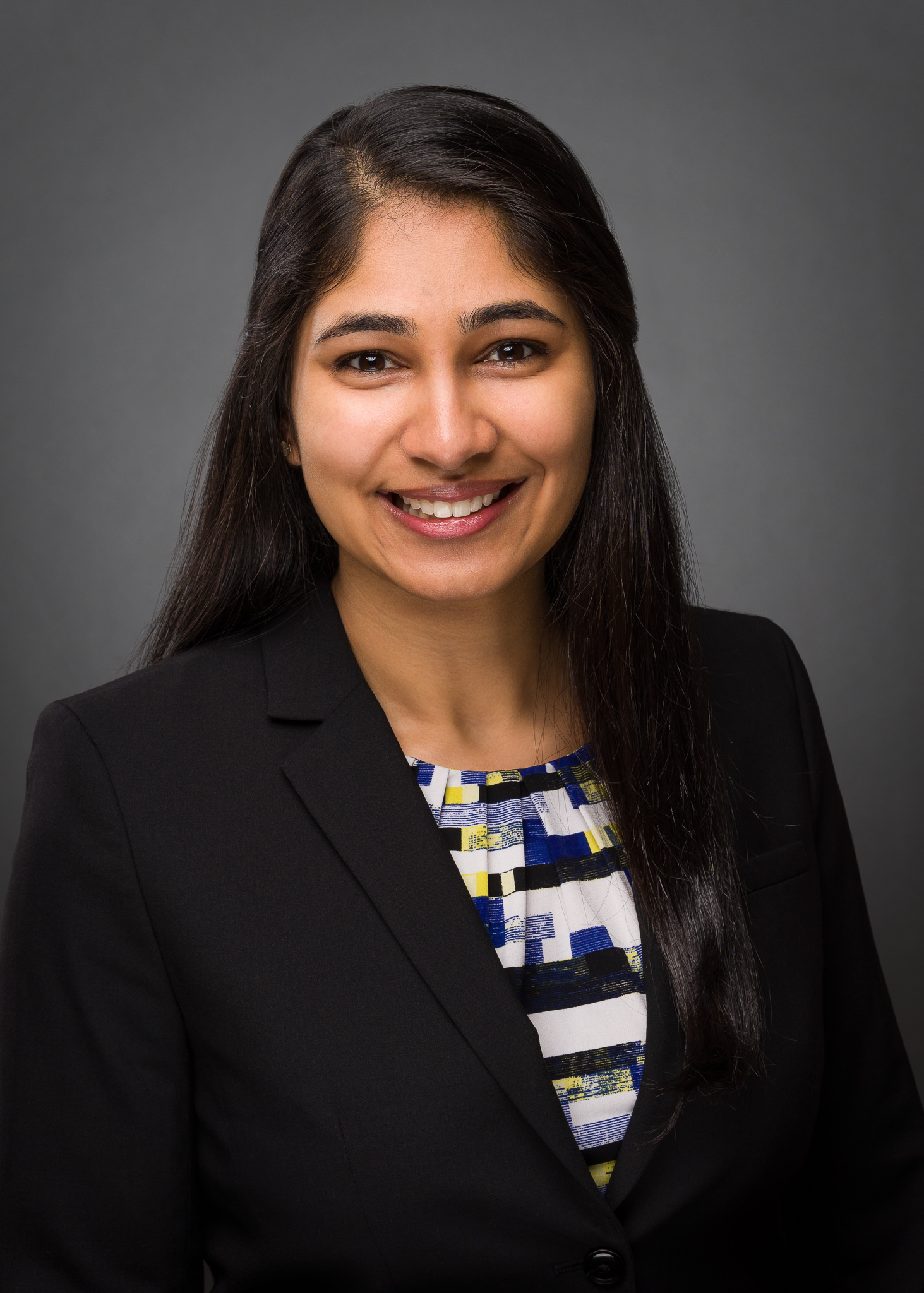 A head and upper torso headshot of a South Asian young woman wearing business attire.