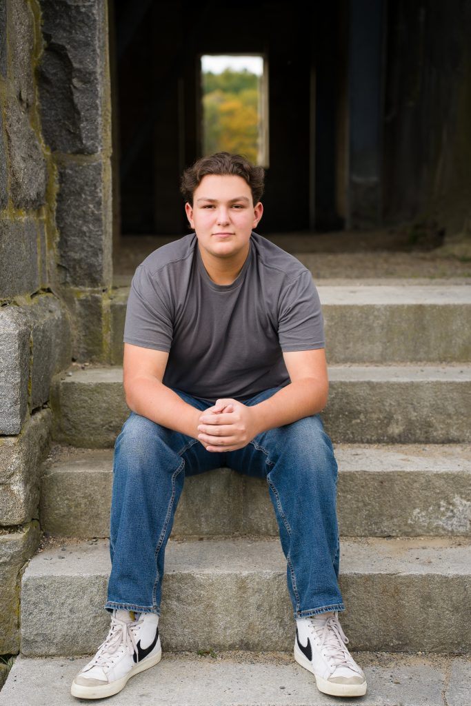 High school boy sitting on steps of a stone building, senior portrait session in Boylston, MA.