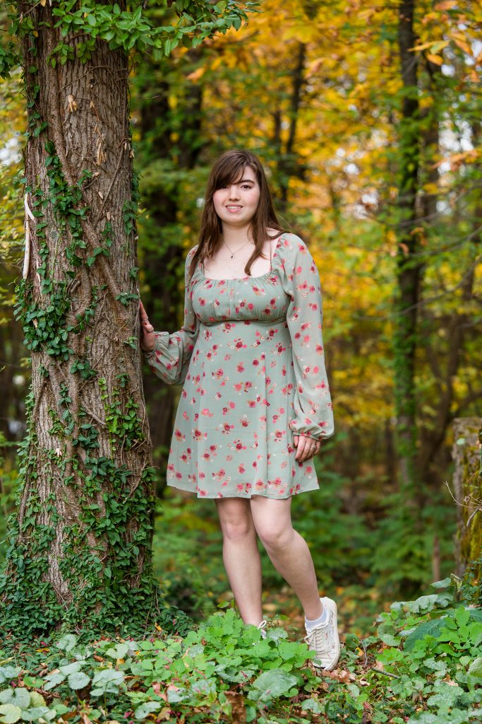 Senior girl in a floral dress leaning against a vine-covered tree, fall senior portrait in Garden of Sweet Remembrance, Shrewsbury, MA
