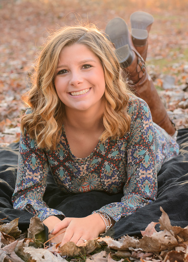 Senior girl smiling while lying on fall leaves with boots up, autumn senior portrait in Moore State Park, Paxton, MA