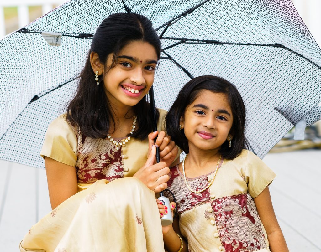 Two young South Asian girls sitting under an umbrella, family portrait session in Northborough, MA.