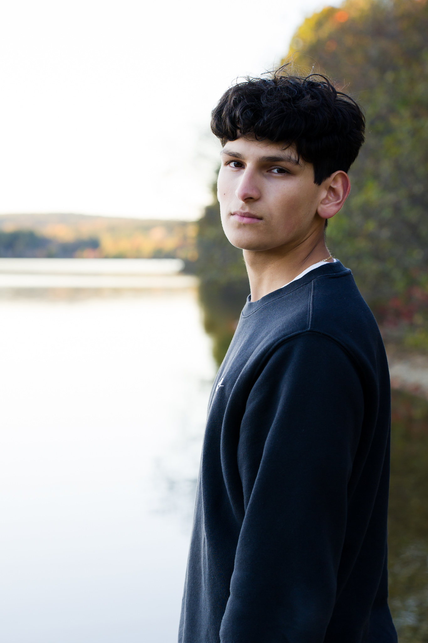 Senior guy looking over shoulder standing beside water at Old Stone Church, West Boylston MA, no flash