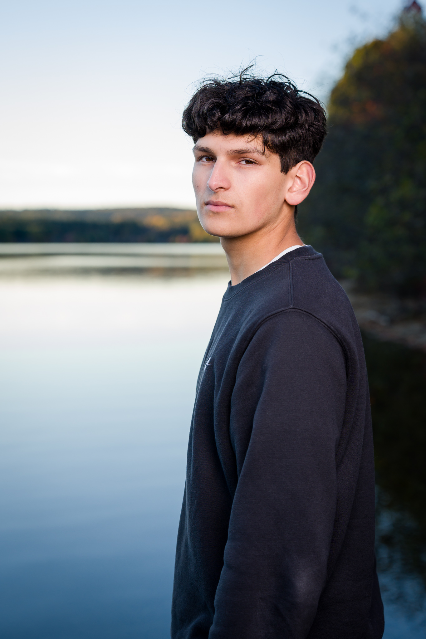 Senior guy looking over shoulder standing beside water at Old Stone Church, West Boylston MA, with flash