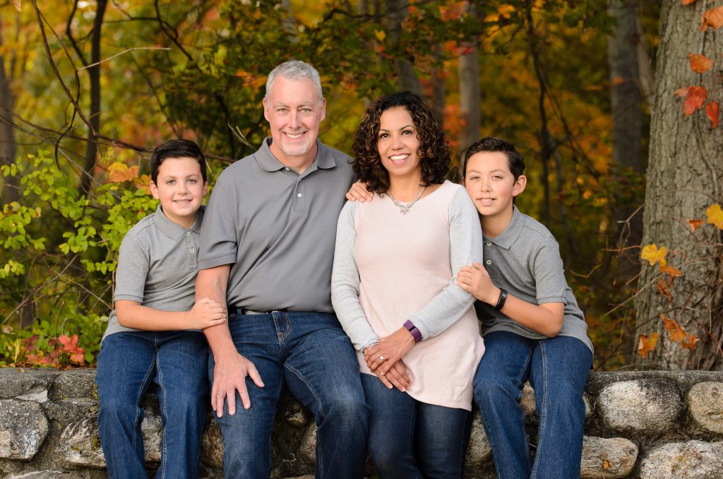Parents and two sons sitting on a stone wall in fall foliage, family portrait in Dean Park, Shrewsbury, MA