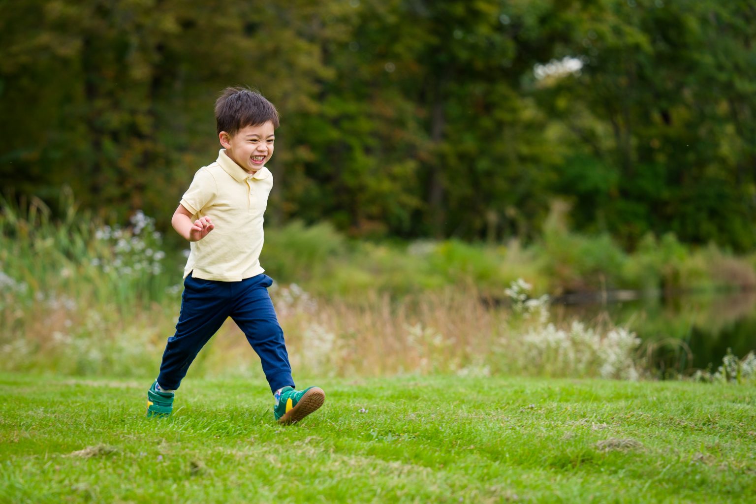 Young boy in a yellow polo laughing and running across the grass, family portrait at Dean Park, Shrewsbury, MA